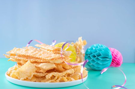 Sfrappole or chiachiere or angel wings on a bright blue background. Italian Carnival and TYPICAL food. Traditional sweet crisp pastry deep-fried and sprinkled . Copy space