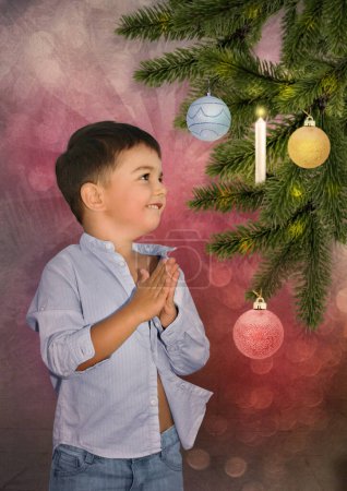 Téléchargez les photos : Petit garçon avec un sourire sur le visage regardant un arbre de Noël avec des jouets - en image libre de droit