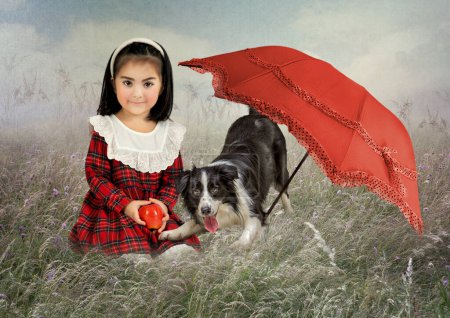 Photo for A little girl with an apple in her hands, sitting in the rye in a field, and a dog under a red umbrella - Royalty Free Image