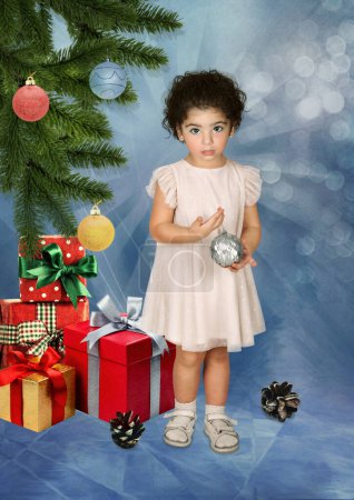 Téléchargez les photos : Une petite fille avec une boule de Noël dans ses mains entourée de cadeaux du Nouvel An sous le sapin de Noël - en image libre de droit