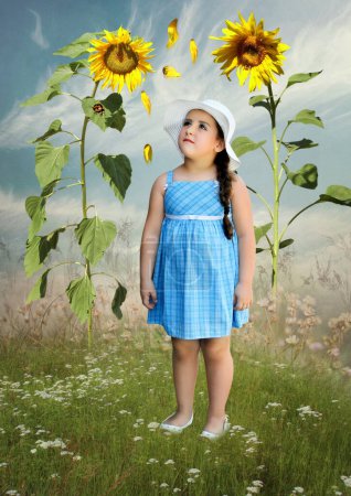 Foto de Una niña con un sombrero blanco en un campo mirando girasoles y pétalos voladores - Imagen libre de derechos