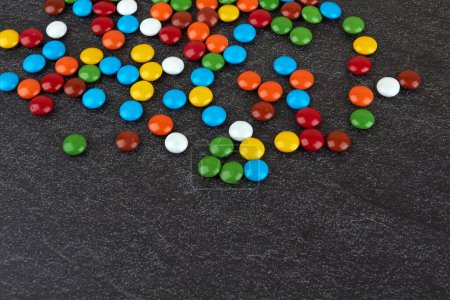 Colorful chocolate buttons on bkack stone surface