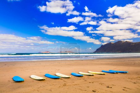 Foto de Tablas de surf en la amplia playa de arena Famara - famosa playa de surf en Lanzarote, Islas Canarias - Imagen libre de derechos