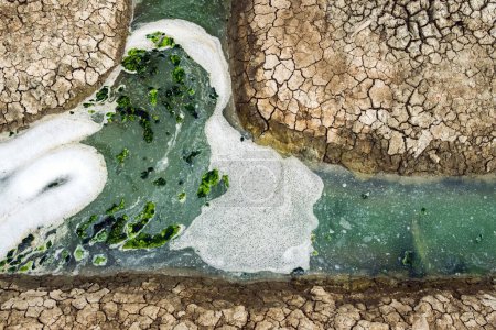 Foto de Top view of wastewater with air bubbles and moss flowing through a cracked ditch. Oxygen bubble in dirty sewage water treatment in a water filled ditch. The surface of the effluent has air bubbles. - Imagen libre de derechos