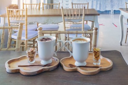 Photo for Hot cappuccino and Ovaltine with small biscuits on wooden tray on wooden table in cafe with table and chair in background. Hot coffee and Ovaltine with bread for afternoon snacks.Good nutrition health - Royalty Free Image