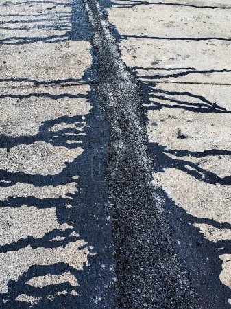 Asphalte sur la route. Rue avec du goudron noir remplissant les fissures. Les fissures dans la surface du béton sont ensuite remplies d'asphalte. Texture de la vieille route asphaltée. L'asphalte est recouvert de fissures, remplies de goudron.
