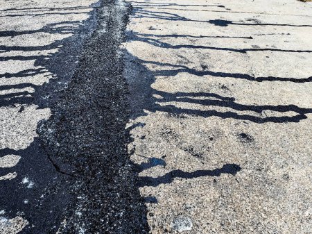 Asphalte sur la route. Rue avec du goudron noir remplissant les fissures. Les fissures dans la surface du béton sont ensuite remplies d'asphalte. Texture de la vieille route asphaltée. L'asphalte est recouvert de fissures, remplies de goudron.