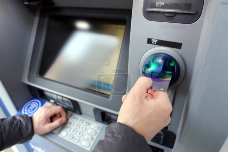 Téléchargez les photos : Un homme faisant une transaction avec une carte de crédit à un distributeur automatique de billets - en image libre de droit