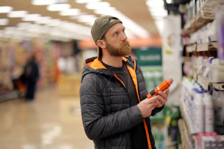 Téléchargez les photos : Un client masculin s'intéresse à une bouteille de déodorant de couleur orange à l'épicerie pour le traitement de la couche d'ozone - en image libre de droit