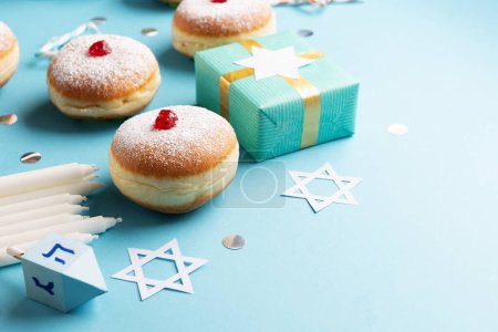 Photo for Hanukkah sweet doughnuts sufganiyot (traditional donuts) with fruit jelly jam, gift boxes, spinnig driedel and white candles on blue paper background. Jewish holiday Hanukkah concept, copy space. - Royalty Free Image