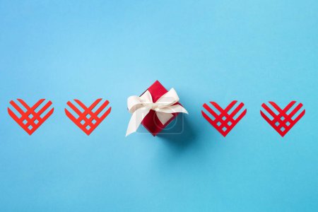 Giving Tuesday, global day of charitable giving after Black Friday shopping day. Charity, give help, donations support concept. Red paper hearts and gift box on blue background. Top view, copy space.