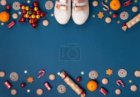 Photo for Saint Nicholas Day, 6 December. Christmas card with children's shoes, sweets, candy, gingerbread cookies, gifts on blue background, top view. Traditional winter holiday in Germany and Western Europe. - Royalty Free Image
