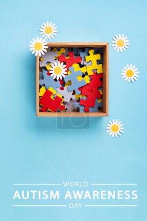 Téléchargez les photos : Journée mondiale de sensibilisation à l'autisme ou concept de mois. Design créatif pour le 2 avril. Puzzle de couleur, symbole de sensibilisation aux troubles du spectre autistique et aux fleurs de marguerite sur fond bleu. Vue du dessus, espace de copie. - en image libre de droit