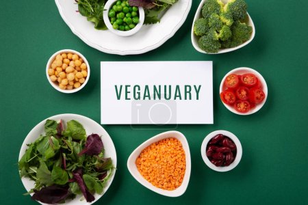 Vegetarian and vegan diet month in january called Veganuary. Variety of vegan, plant based protein food, healthy raw vegetables. Top view on green background.