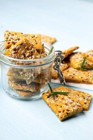 Gluten free Homemade Crackers and rosemary on Blue background. Healthy eating, ancient grain food, dieting, balanced food concept. Cereals gluten-free, millet, quinoa, flax seeds, sunflower seeds.
