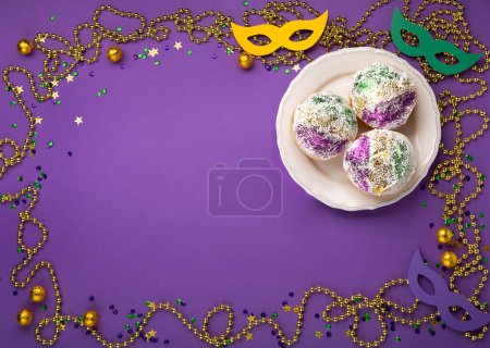 Photo for Mardi Gras King Cake sufganiyot donuts, masquerade festival carnival masks, gold beads and golden, green, purple confetti on purple background. Holiday party invitation, greeting card concept. - Royalty Free Image