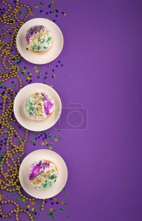 Photo for Mardi Gras King Cake sufganiyot donuts, masquerade festival carnival gold beads and golden, green, purple confetti on purple background. Holiday party invitation, greeting card concept. - Royalty Free Image