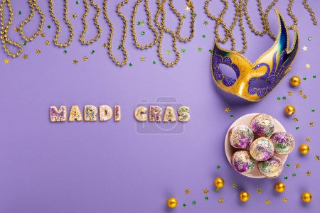 Téléchargez les photos : Mardi Gras King Cake cupcake or muffins, masquerade festival carnival mask, gold beads and golden, green confetti on purple background. Holiday party invitation, greeting card concept. - en image libre de droit