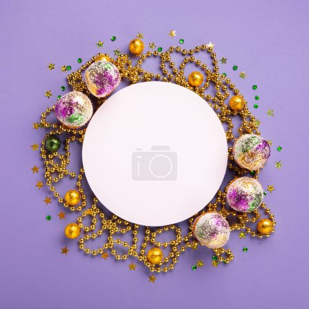 Photo for Mardi Gras King Cake cupcake or muffins, masquerade festival carnival mask, gold beads and golden, green confetti on purple background. Holiday party invitation, greeting card concept. - Royalty Free Image