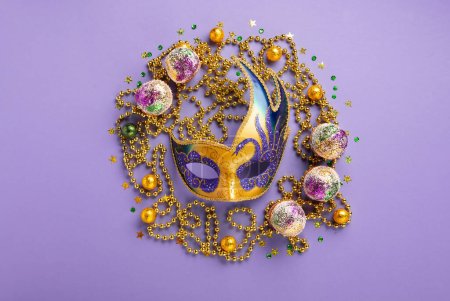 Photo for Mardi Gras King Cake cupcake or muffins, masquerade festival carnival mask, gold beads and golden, green confetti on purple background. Holiday party invitation, greeting card concept. - Royalty Free Image