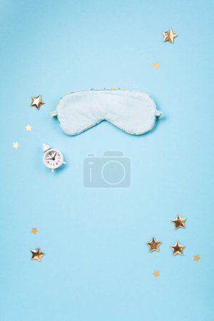Téléchargez les photos : World Sleep day observed on March. Quality of sleep, good night, insomnia, relaxation concept. Sleeping mask, golden stars and white alarm clock on blue background. Flat lay, top view - en image libre de droit