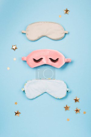 Foto de World Sleep day observed on March. Quality of sleep, good night, insomnia, relaxation concept. Sleeping masks, golden stars and white alarm clock on blue background. Flat lay, top view - Imagen libre de derechos