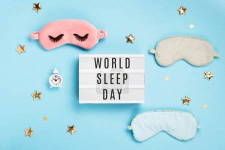 Téléchargez les photos : World Sleep day observed on March. Quality of sleep, good night, insomnia, relaxation concept. Sleeping masks, golden stars and white alarm clock on blue background. Flat lay, top view - en image libre de droit