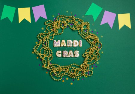 Photo for Mardi Gras King Cake ccookies, masquerade festival carnival mask, gold beads and golden, green, purple confetti on green background. Holiday party invitation, greeting card concept. - Royalty Free Image
