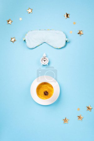 Téléchargez les photos : World Sleep day observed on March. Quality of sleep, good night, insomnia, relaxation concept. Sleeping mask, Turmeric golden milk latte and white alarm clock on blue background. Flat lay, top view - en image libre de droit