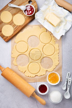 Foto de Making homemade Triangular pastry, Hamantaschen cookies for Purim. Purim celebration, jewish carnival holiday concept. Dough, jam, sugar, butter and rolling pin on gray stone table. Top view, flat lay, copy space. - Imagen libre de derechos