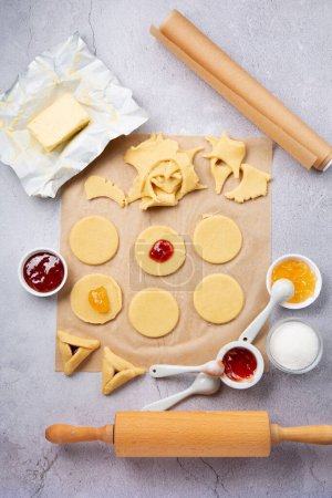 Photo for Making homemade Triangular pastry, Hamantaschen cookies for Purim. Purim celebration, jewish carnival holiday concept. Dough, jam, sugar, butter and rolling pin on gray stone table. Top view, flat lay, copy space. - Royalty Free Image
