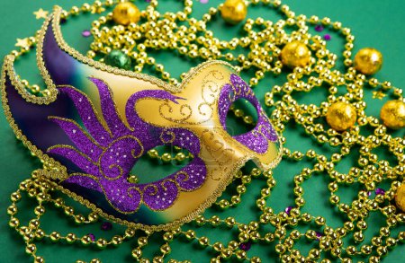 Photo for Mardi Gras masquerade festival carnival mask, gold beads and golden, green, purple confetti on green background. Holiday party invitation, greeting card concept. - Royalty Free Image