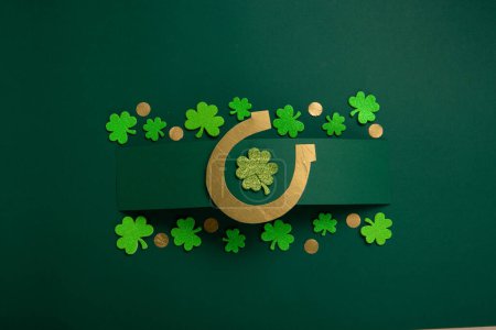 Téléchargez les photos : St. Patrick's Day celebration Concept. Greeting card with traditional symbols - Golden horseshoe, gold coins and clover leaves, green shamrocks on green background. Top view, copy space. - en image libre de droit