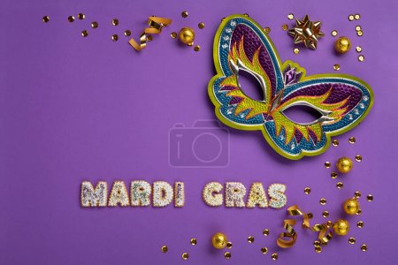 Téléchargez les photos : Mardi Gras masquerade festival carnival Mask, chocolate candies in foil, gold beads and golden confetti on purple background. Holiday party invitation, greeting card concept. - en image libre de droit