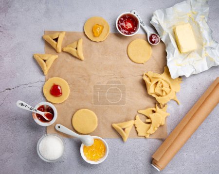 Téléchargez les photos : Making homemade Triangular pastry, Hamantaschen cookies for Purim. Purim celebration, jewish carnival holiday concept. Dough, jam, sugar, butter and rolling pin on gray stone table, Top view. - en image libre de droit