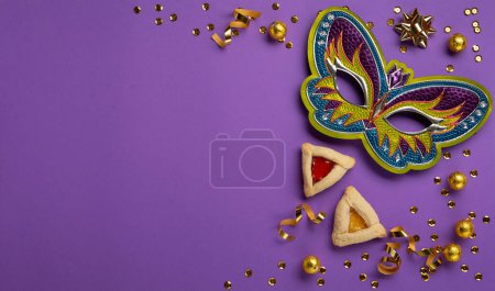 Photo for Purim celebration jewish carnival holiday concept. Tasty hamantaschen cookies, Triangular pastry, Festive carnival mask, sweet chocolte candies and party decor on purple Background. Top view, copy space. - Royalty Free Image