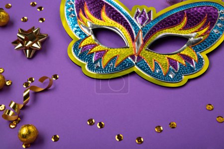 Foto de Mardi Gras masquerade festival carnival Mask, chocolate candies in foil, gold beads and golden confetti on purple background. Holiday party invitation, greeting card concept. - Imagen libre de derechos