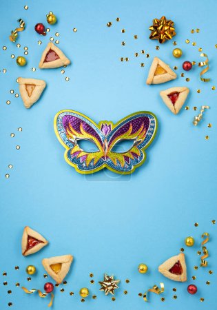 Photo for Purim celebration jewish carnival holiday concept. Tasty hamantaschen cookies, Carnival mask, sweet chocolate candies and party decor on blue background. Top view, flat lay, copy space. - Royalty Free Image