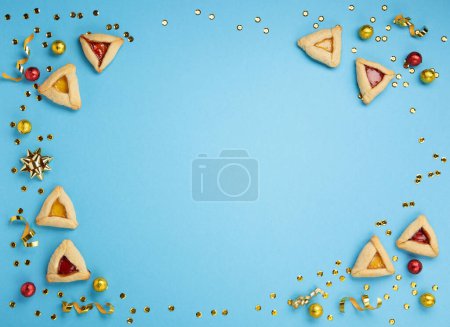 Téléchargez les photos : Purim celebration jewish carnival holiday concept. Tasty hamantaschen cookies, sweet candies and Carnival party decor on blue background. Top view, flat lay, copy space. - en image libre de droit