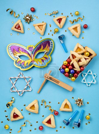 Photo for Purim celebration jewish carnival holiday concept. Tasty hamantaschen cookies, Carnival mask, noisemaker, sweet candies and party decor on blue background. Top view, flat lay, copy space. - Royalty Free Image