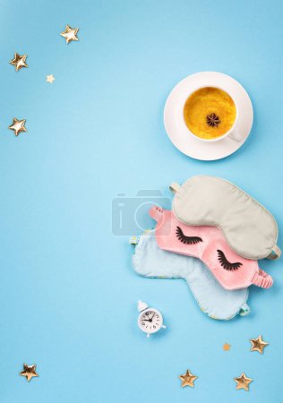 Foto de World Sleep day observed on March. Quality of sleep, good night, insomnia, relaxation concept. Sleeping mask, Turmeric golden milk latte and white alarm clock on blue background. Flat lay, top view - Imagen libre de derechos