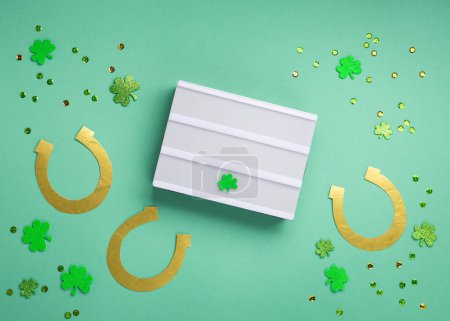 Foto de St. Patrick's Day celebration Concept. Greeting card with traditional symbols - Golden horseshoes, gold coins and clover leaves, green shamrocks on green mint background. Top view, copy space. - Imagen libre de derechos