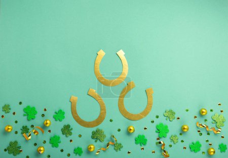 Foto de St. Patrick's Day celebration Concept. Greeting card with traditional symbols - Golden horseshoes, gold coins and clover leaves, green shamrocks on green mint background. Top view, copy space. - Imagen libre de derechos