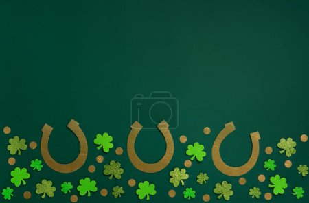 Téléchargez les photos : St. Patrick's Day celebration Concept. Greeting card with traditional symbols - Golden horseshoes, gold coins and clover leaves, green shamrocks on green background. Top view, copy space. - en image libre de droit