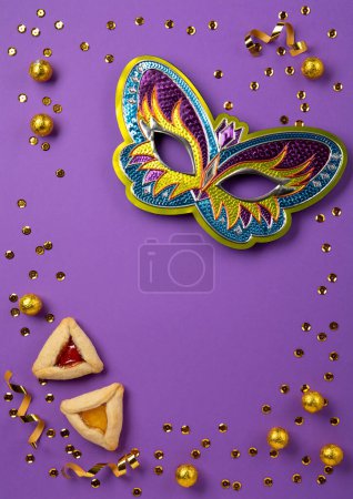 Foto de Purim celebration jewish carnival holiday concept. Tasty hamantaschen cookies, Triangular pastry, Festive carnival mask, noisemaker, sweet candies and party decor on purple Background. Top view, flat lay, copy space. - Imagen libre de derechos