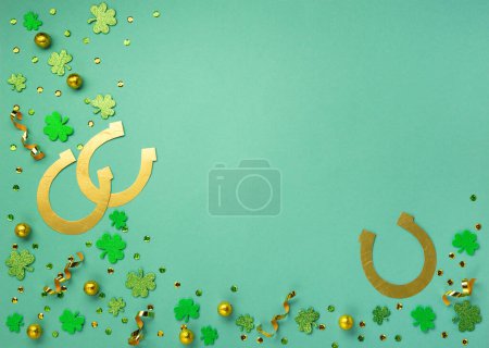Téléchargez les photos : St. Patrick's Day celebration Concept. Greeting card with traditional symbols - Golden horseshoe, gold coins and clover leaves, green shamrocks on green mint background. Top view, copy space. - en image libre de droit