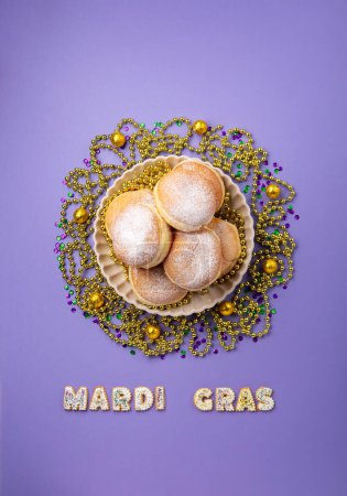 Photo for Mardi Gras King Cake doughnuts or donuts, chocolates candies, gold beads and golden, green confetti on purple background. Holiday party invitation, greeting card concept. - Royalty Free Image