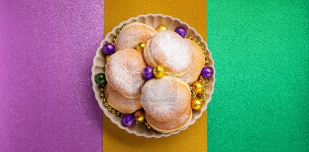 Foto de Mardi Gras King Cake doughnuts or donuts, gold beads and golden chocolate candies on purple background. Holiday party invitation, greeting card concept. - Imagen libre de derechos