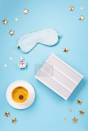 Téléchargez les photos : World Sleep day observed on March. Quality of sleep, good night, insomnia, relaxation concept. Sleeping mask, Turmeric golden milk latte and white alarm clock on blue background. Flat lay, top view - en image libre de droit
