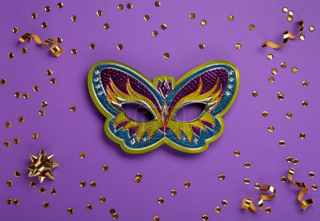 Photo for Mardi Gras masquerade festival carnival mask, gold beads and golden, green confetti on purple background. Holiday party invitation, greeting card concept. - Royalty Free Image